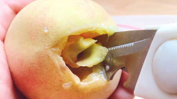 キッチンはさみを使って桃の種を取ります